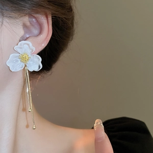Elegant acrylic white flower earrings with long gold tassels on a model for a chic look