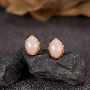 Close-up of S925 silver oval pink jade stud earrings on a dark textured stone base