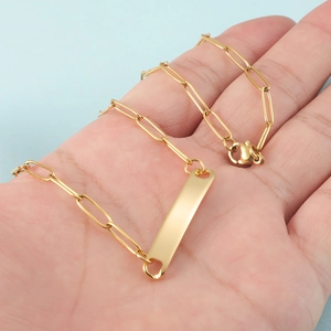 Hand holding a gold paperclip chain necklace with a sleek rectangular polished pendant