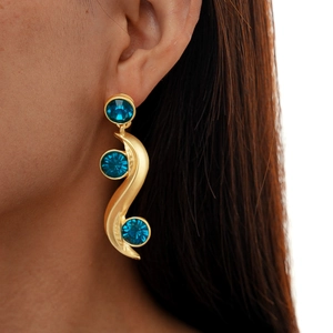 Close-up of golden wavy earrings with three round dark blue crystal gems on female model