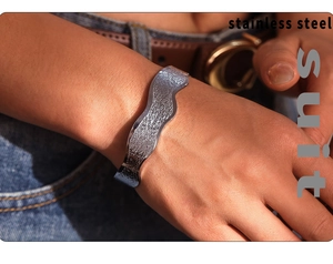 Detailed close-up of a wavy textured stainless steel open bangle worn on a female wrist