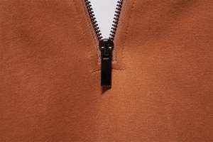 Detail of the metal zipper and black slider on the rust brown long sleeve polo sweatshirt
