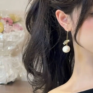 Elegant gold leaf pearl drop earrings worn by a model in a cozy indoor setting