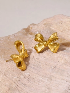 Gros plan sur des boucles d'oreilles nœud dorées sur fond de pierre naturelle