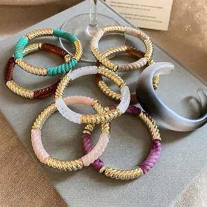 Golden twisted bangle with colorful acrylic inlay displayed in a luxury jewelry box