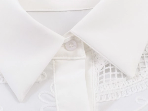 Detailed macro view of white cotton shirt collar with elegant lace embroidery and buttons