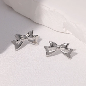 Macro shot of minimalist silver bow stud earrings on a textured stone surface