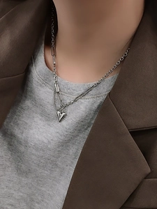 Gros plan d'un collier cœur avec chaîne trombone asymétrique sur un tissu gris