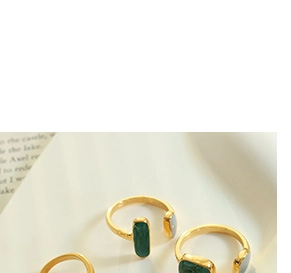 Close-up of golden open rings featuring rectangular green gemstones on book pages