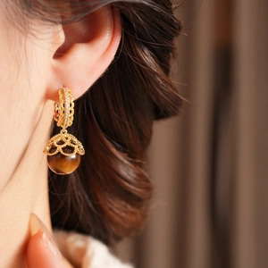 Macro shot of gold-plated tiger eye drop earrings with zircon on a model for a vintage look