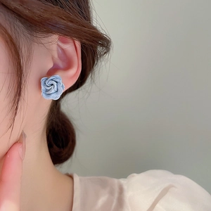 Close-up of matte grey-blue rose stud earrings with layered petals on model