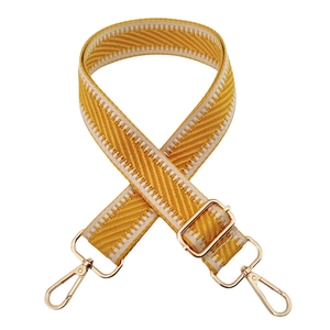 Close-up of yellow and white herringbone woven strap with adjustable gold buckles