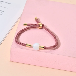 Detail of adjustable pink braided rope bracelet with a white heart stone charm