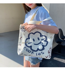 Detail of white canvas tote bag featuring blue cloud patterns and wide shoulder straps