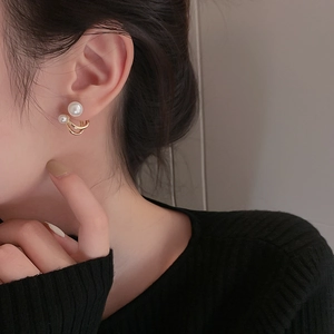 Detail view of a gold-finish C-shape earring with pearls on a model ear