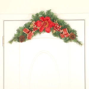 Red Christmas swag with pine needles, poinsettia, and berries hanging on a white door