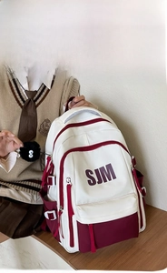 Detail of college style backpack with SJM logo, multi-pocket design, and plush charm