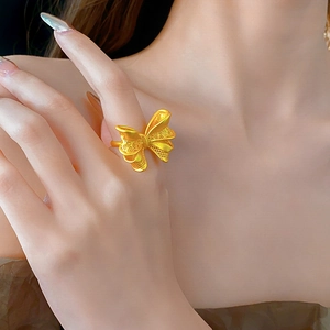 Detail of matte gold bow ring on finger featuring intricate openwork filigree design
