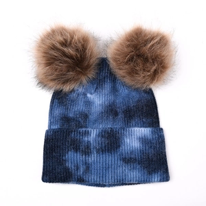 Détail du bonnet en tricot tie-dye bleu avec doubles pompons duveteux sur fond blanc