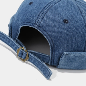 Détail du bonnet miki en jean bleu montrant les coutures blanches et la boucle en laiton