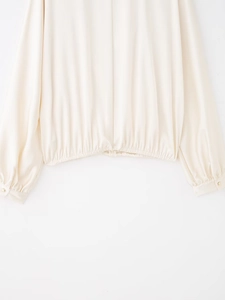Détail d'un chemisier en satin crème avec ourlet élastique et bouton doré au poignet