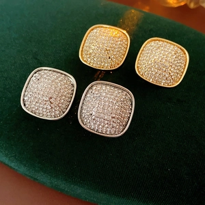 Macro shot of square pave rhinestone earrings in gold and silver on green velvet