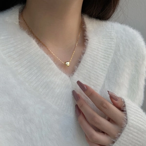 Close-up of a delicate gold heart pendant necklace on a model wearing white knitwear