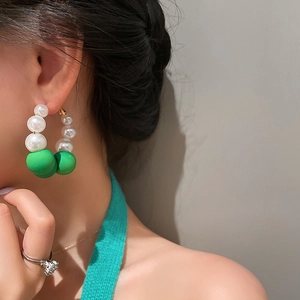 Close-up of model wearing large hoop earrings with white pearls and matte green beads