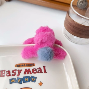 Detail of pink faux fur claw clip with blue pompom on a ceramic plate edge