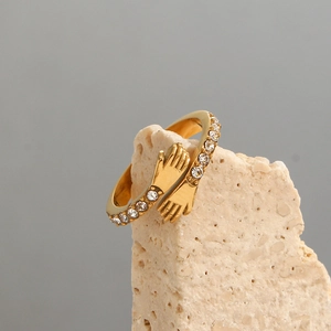 Detailed view of hug hands gold ring with cubic zirconia stones on a beige rock