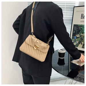 Detail of beige pleated crossbody bag with gold heart clasp worn by a model in a black suit