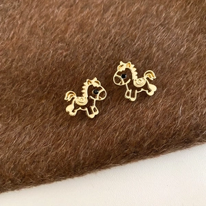 Close-up of golden horse stud earrings with black eye details on brown faux fur