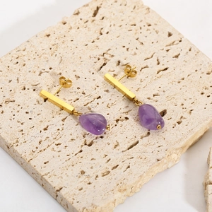 Detailed macro view of 18k gold earrings featuring purple natural stones on travertine