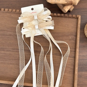 Detailed view of handmade lace bow hair clips with long ribbon tassels on card packaging