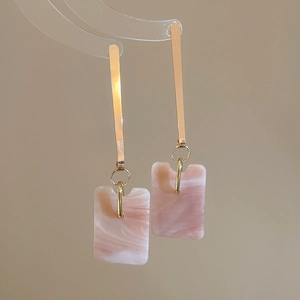 Close-up of gold-plated earrings with rectangular pink marble resin pendants