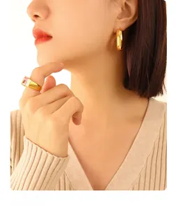 Close-up of a model wearing gold U-shaped earrings and a pink gemstone ring