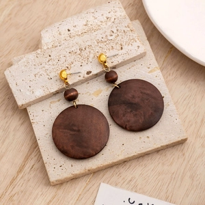 Detailed view of geometric brown wood drop earrings on a light stone and wood background