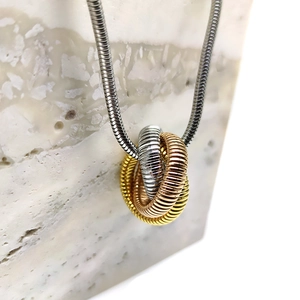 Detailed macro shot of a tricolor interlocking ring pendant on a sleek snake chain