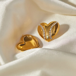 Close-up of gold heart-shaped earrings with rhinestones on white satin fabric