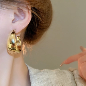 Close-up of a model wearing wide C-shaped gold hoop earrings with a polished mirror finish