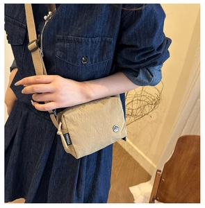 Detail view of khaki nylon crossbody bag on denim outfit showing texture and strap