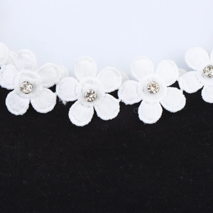 Close-up of white flower embroidery with sparkling rhinestones on black velvet fabric