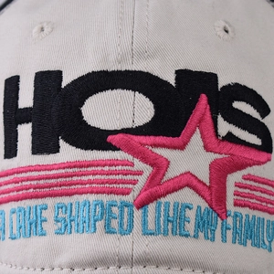 Cotton baseball cap with HOLIS embroidery and pink star, close-up on fabric texture