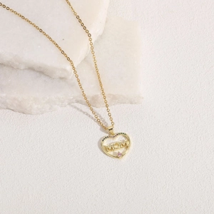Detailed close-up of golden heart MOM pendant with colorful cubic zirconia on white stone