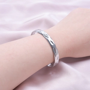 Detail of silver textured open cuff bracelet with hammered design on pink satin fabric