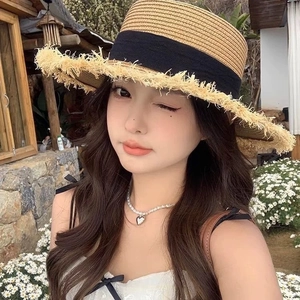 Detail of flat top straw hat with frayed edges and black ribbon bow for summer