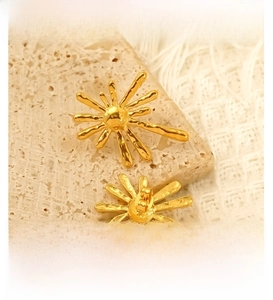 Macro detail of 18K gold-plated irregular sunburst earrings on a textured stone base
