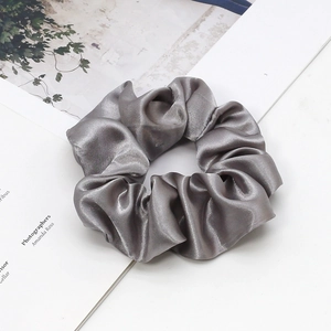Close-up of a grey satin scrunchie with smooth silk texture on minimalist magazine