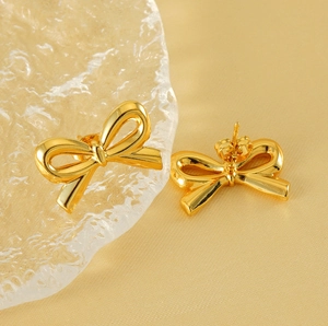 Detailed macro view of 18K gold-plated bow stud earrings on champagne silk background