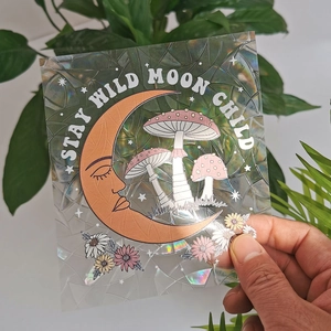Detail showing a holographic suncatcher sticker with a gold crescent moon and mushrooms